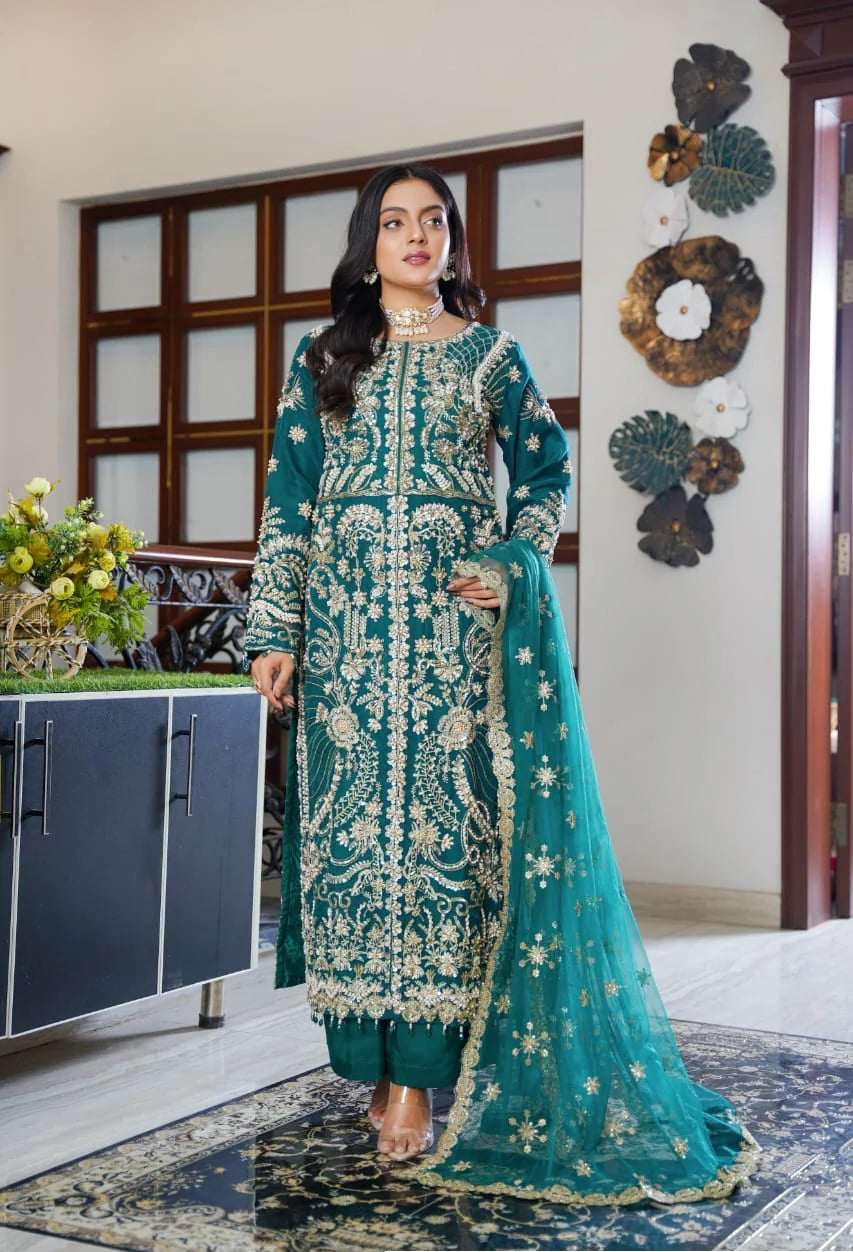 Woman in a teal embroidered traditional outfit standing in a room with decorative elements.